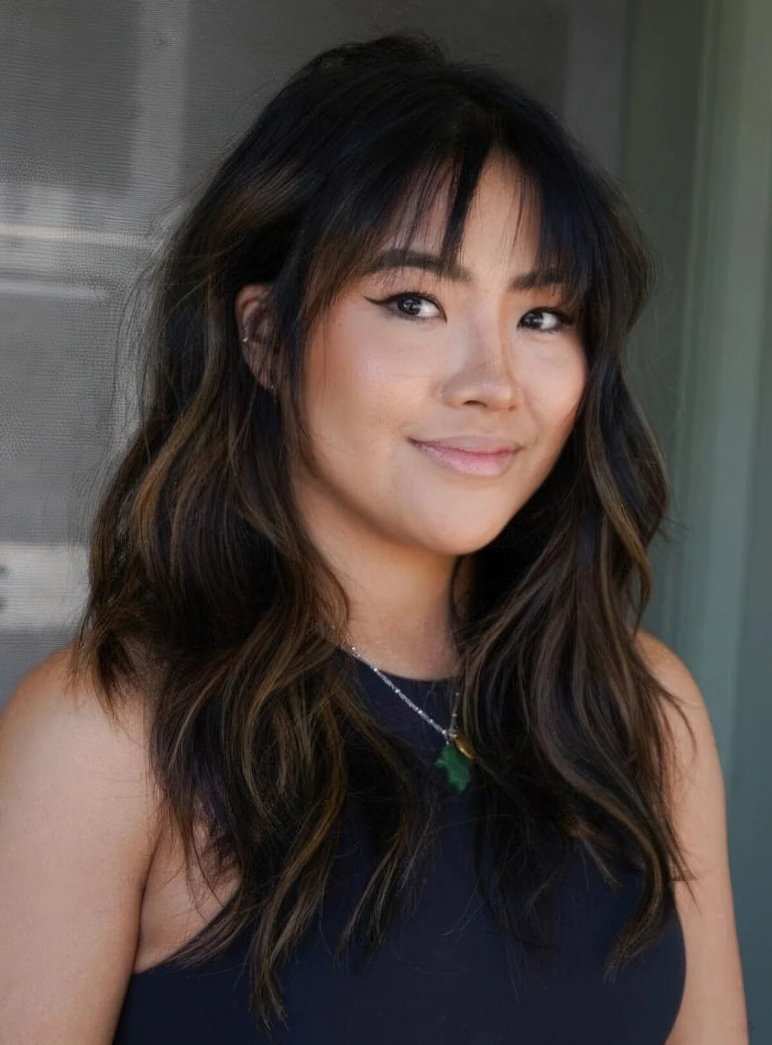 Long black wolf haircut with caramel balayage, wispy bangs and waves.