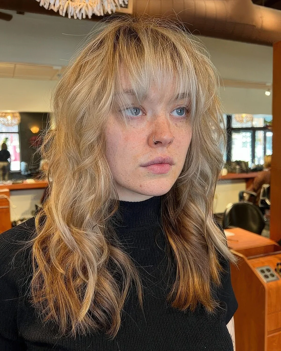 Long blonde wavy wolf cut with outgrown wispy bangs.
