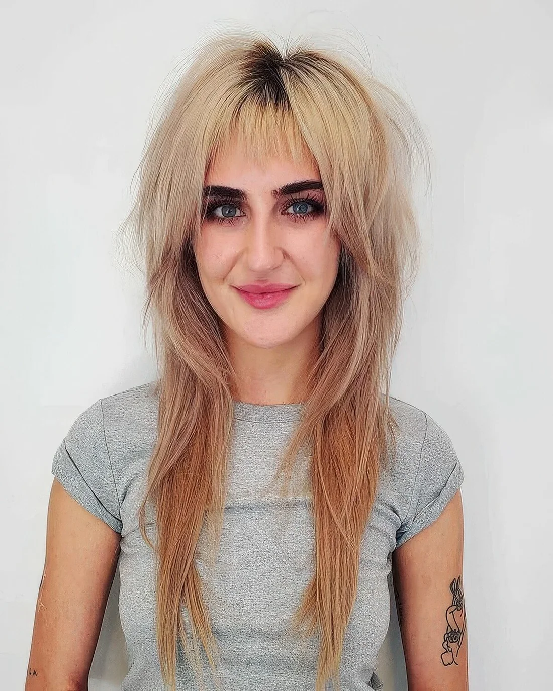 Long blonde wolf haircut with wispy bangs and a darker root.