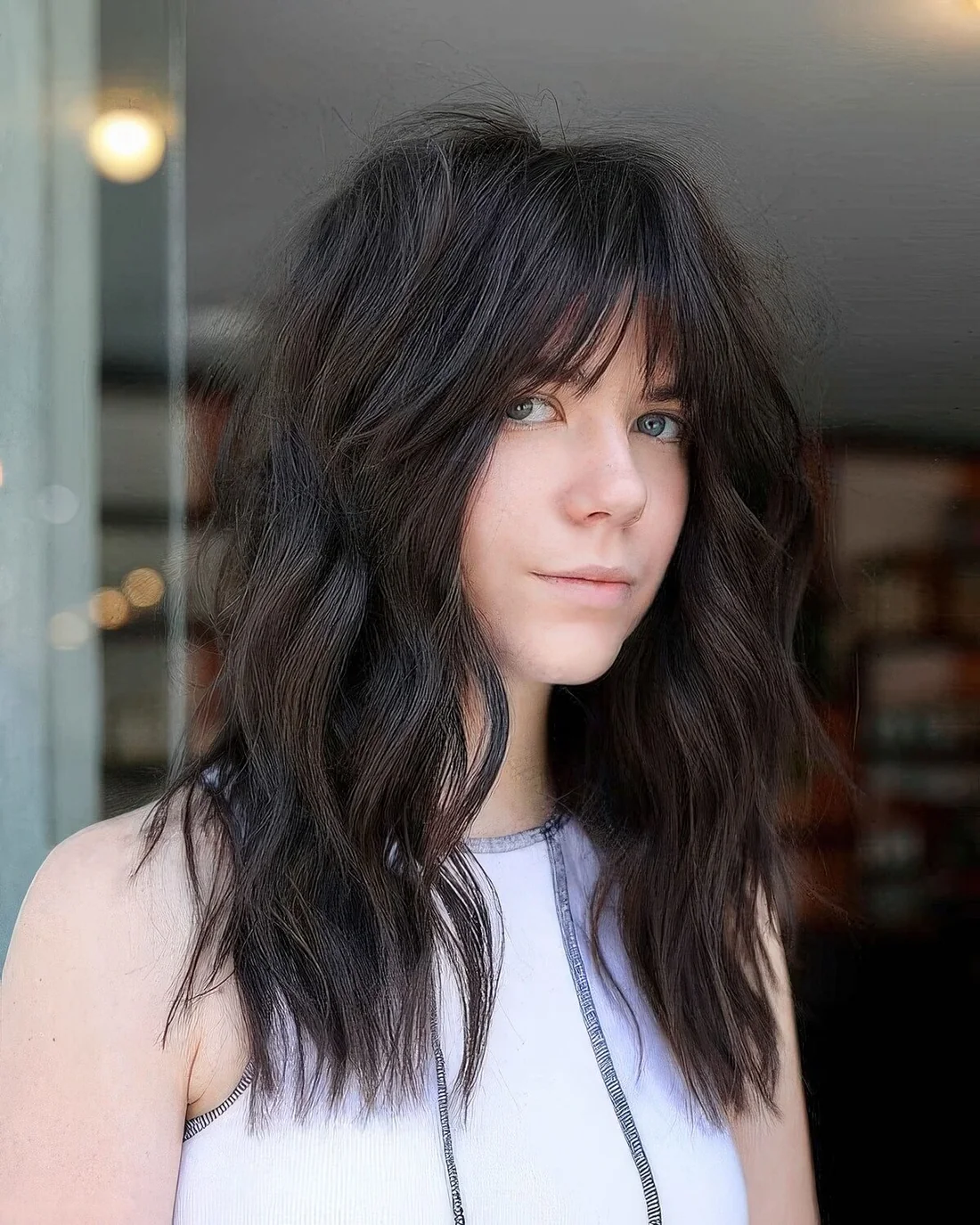 Long dark brown wolf haircut with wispy bangs and messy waves.