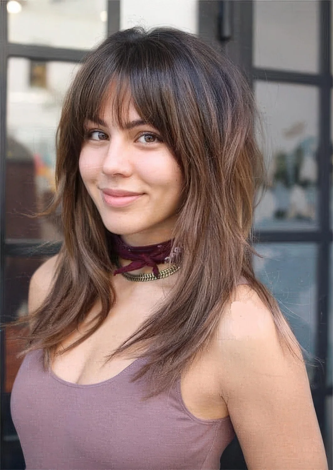 Long brown wolf haircut with caramel balayage and wispy bangs and face-framing layers.