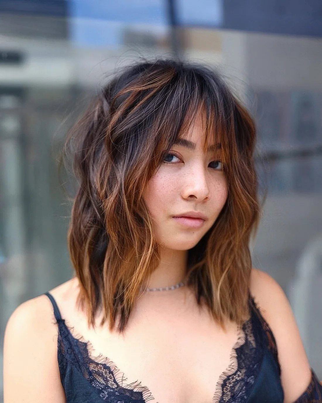 Medium black wolf cut with wispy bangs and caramel balayage and messy waves.