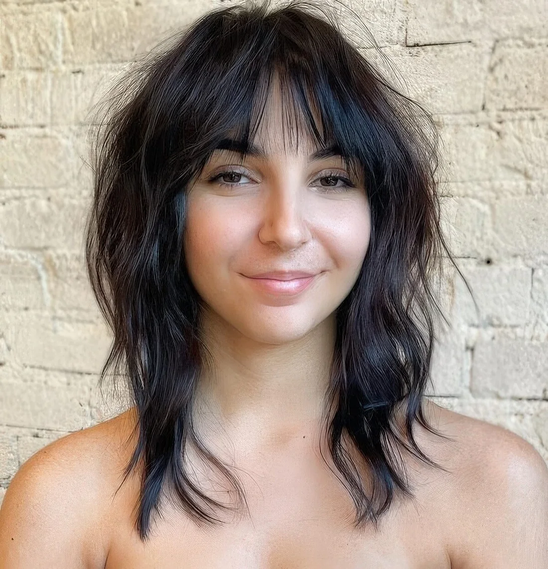 Medium dark brown wolf haircut with wispy bangs and messy waves.