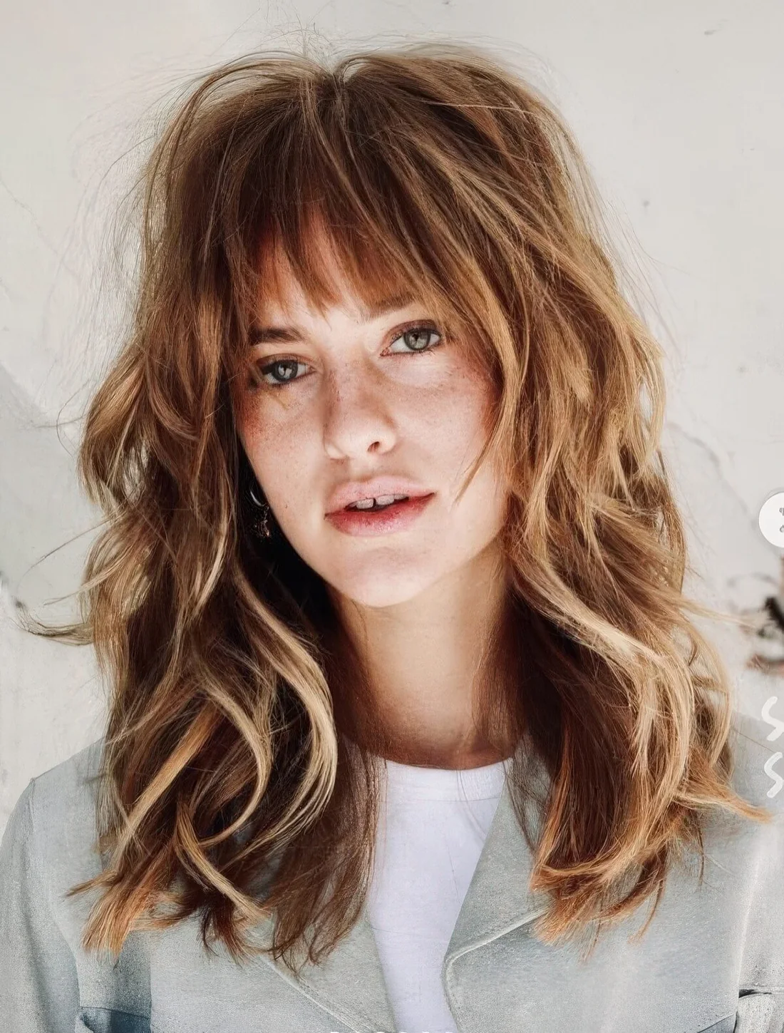 Medium ginger wolf cut with blonde balayage and wispy bangs plus waves.