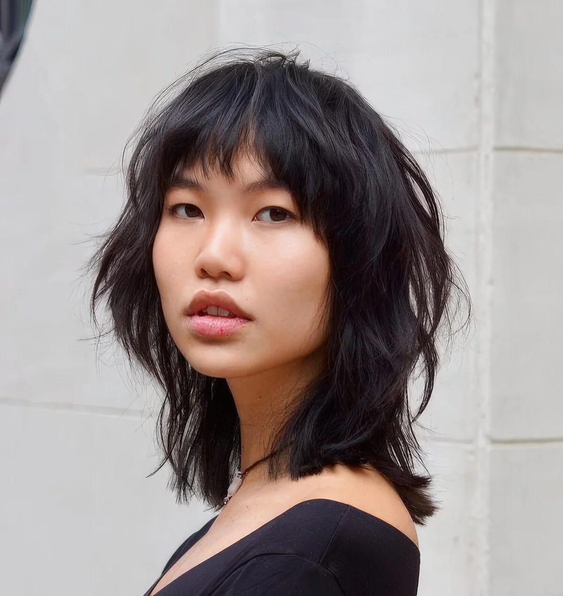 Black wolf cut with bottleneck bangs and messy wavy layers.