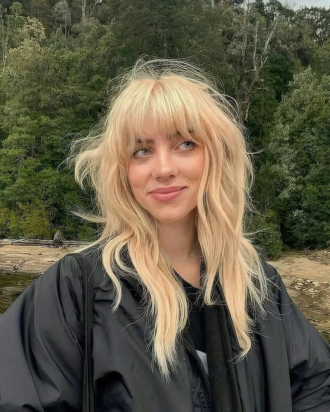 Billie Eilish rocking a blonde wolf cut with outgrown bangs and long layers.