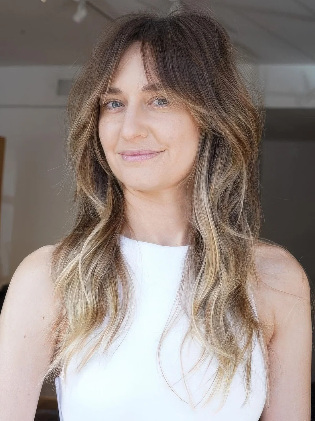Brunette wolf cut with bottleneck bangs and waves down plus blonde balayage.