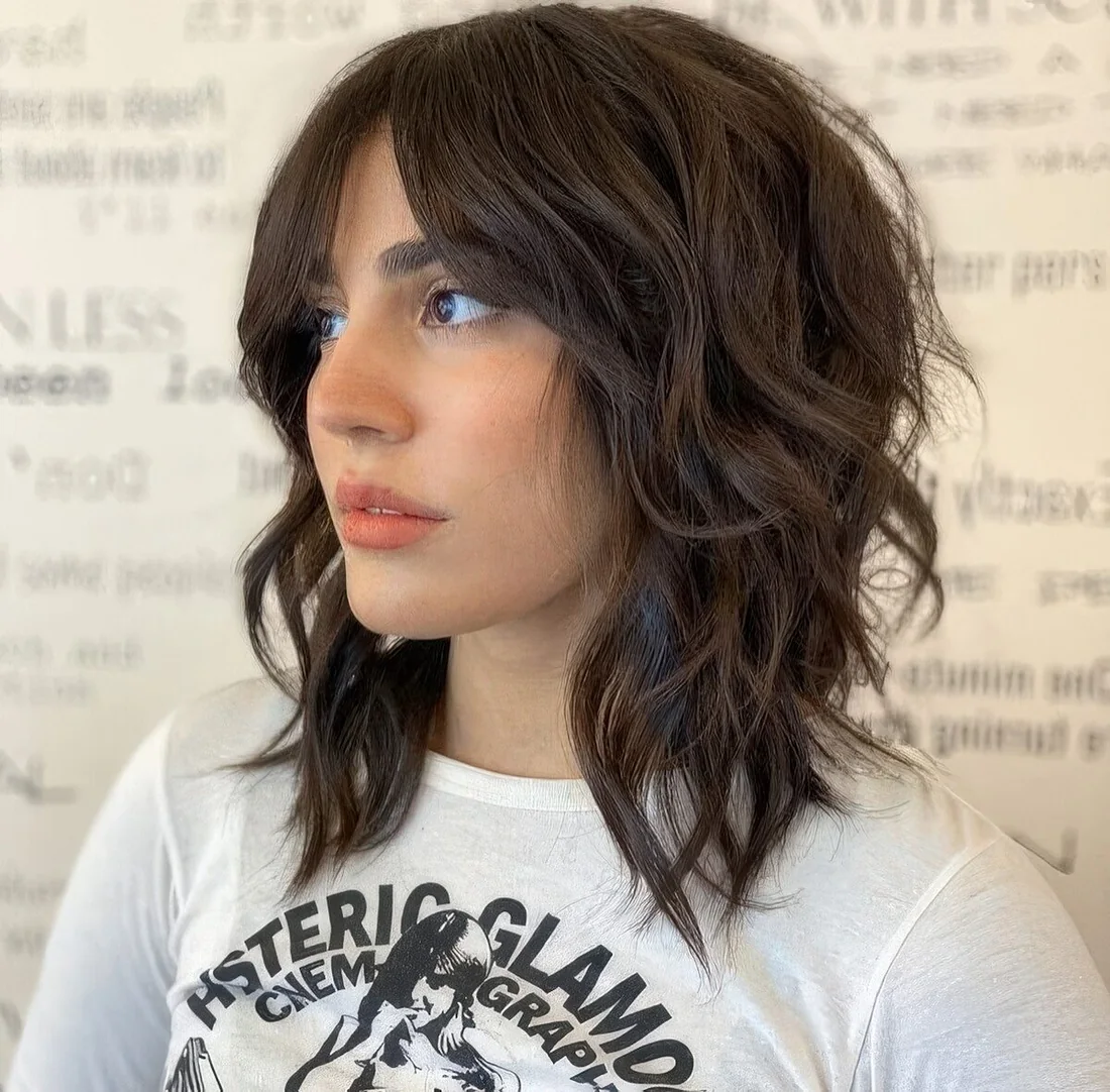 Brown medium wolf cut with waves that make it softer and bottleneck bangs.