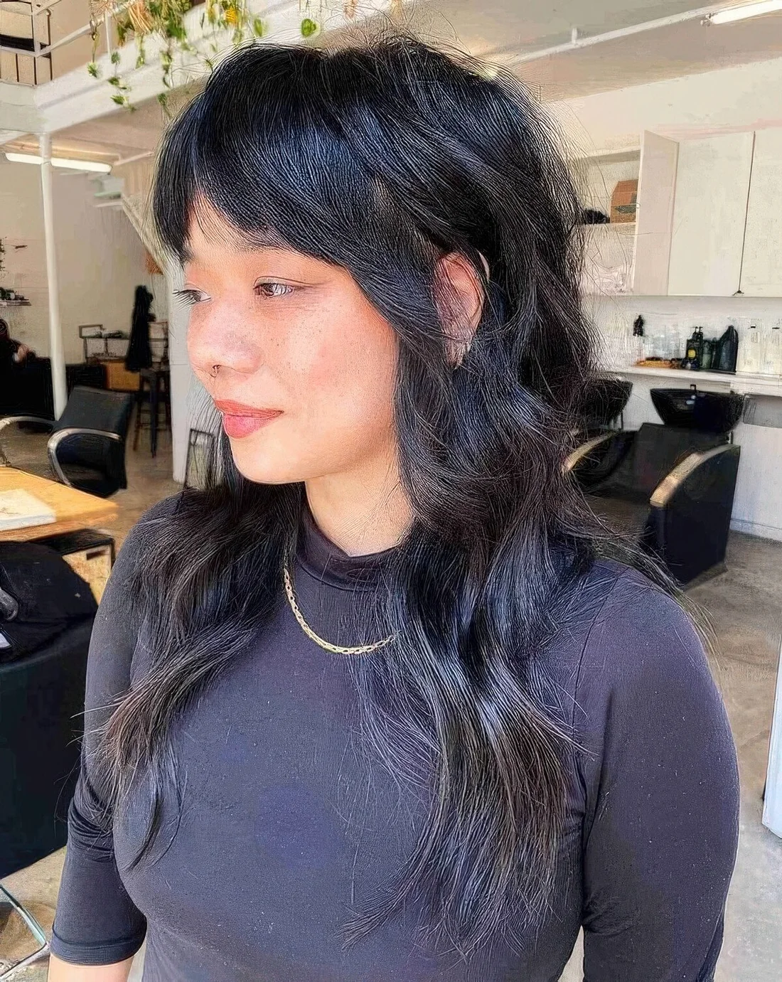 Long black wolf cut with bottleneck bangs and wavy hair with a bit of volume.