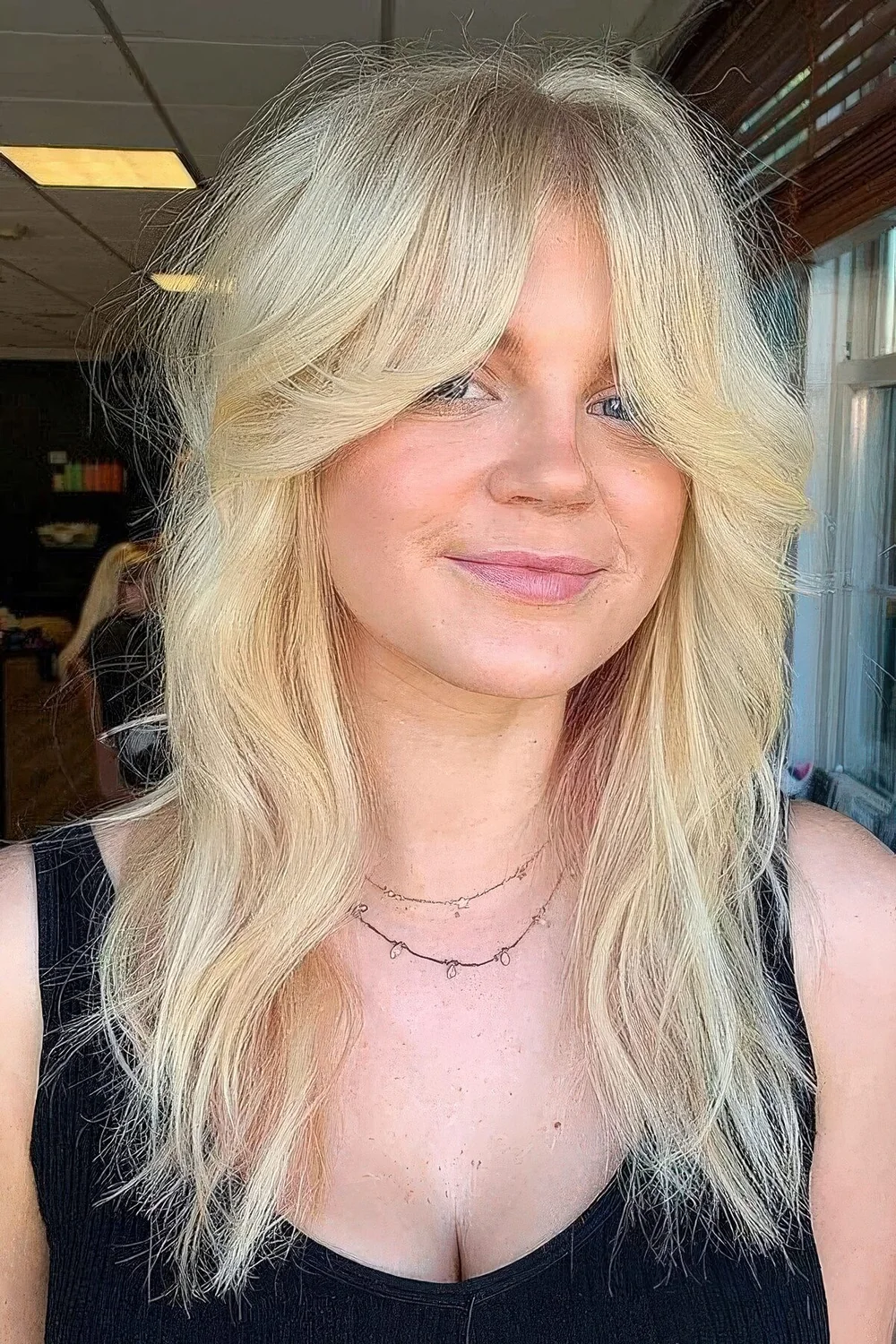 Long blonde wolf cut with bottleneck bangs and textured volume.