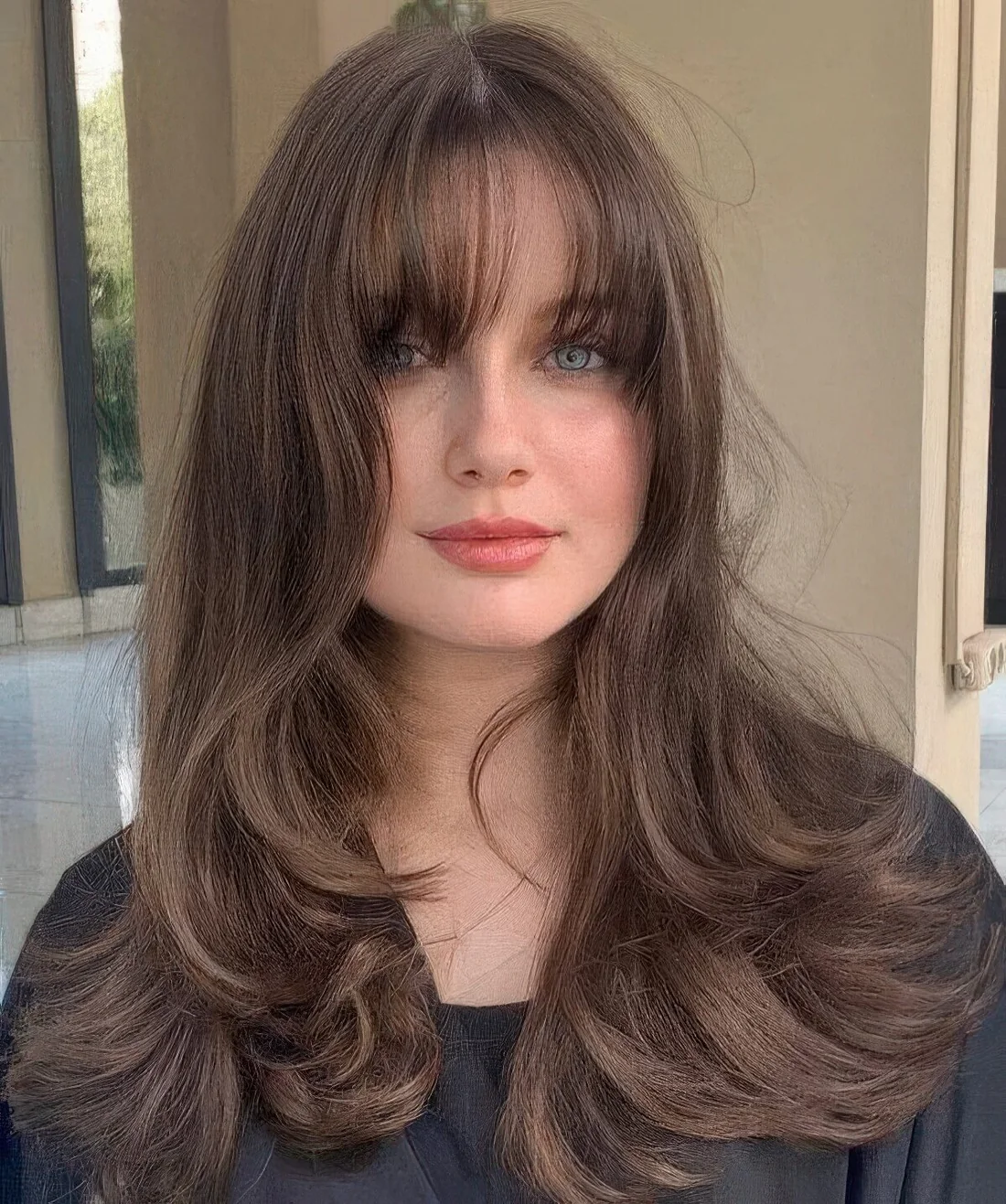 Long brunette wolf cut with bottleneck and wispy bangs and waves.
