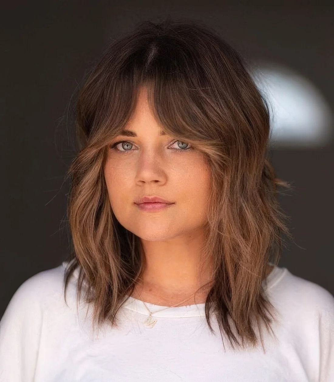 Medium-length wolf cut with caramel balayage and bottleneck bangs plus a bit of messy waves.
