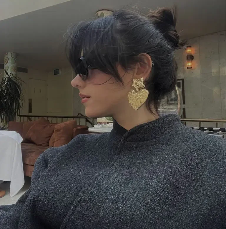 A dark short cut is gathered into a loose mini bun with soft bangs around the eyes