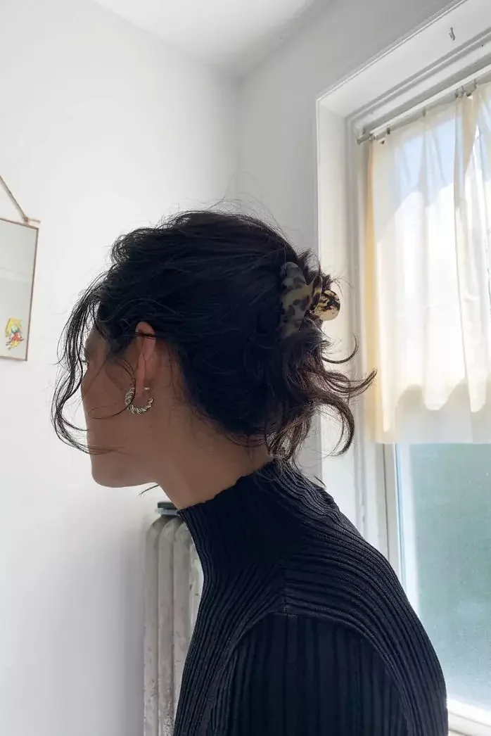 Short dark hair is twisted into a soft low updo with airy pieces at the sides and nape