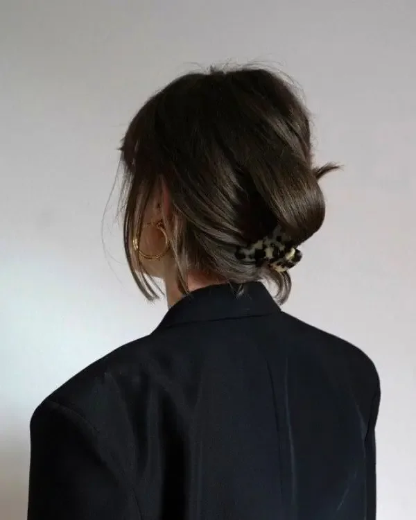 A brunette bob is tucked into a low twist and secured with a small tortoiseshell claw clip