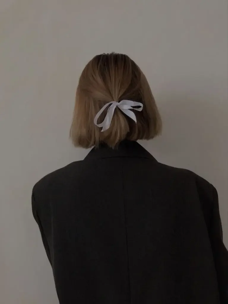 A blunt brunette bob is tied half-up with a narrow gray ribbon at the back