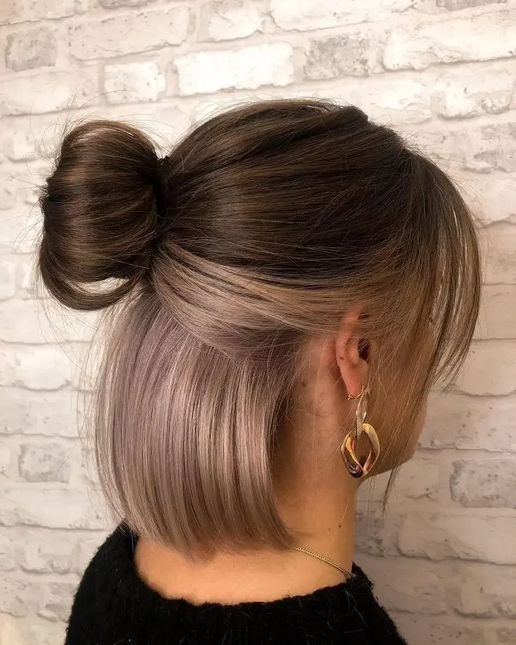 A straight blonde bob is divided cleanly and wrapped into a rounded half-up bun