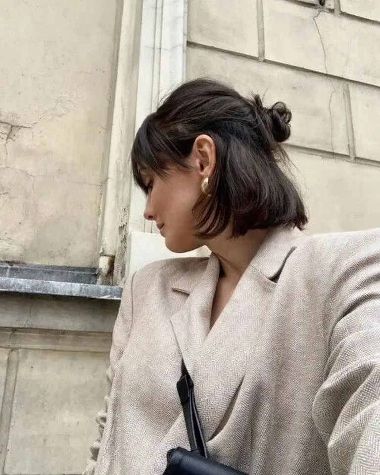 A brunette bob is swept back into a small side-set bun with loose fringe near the face