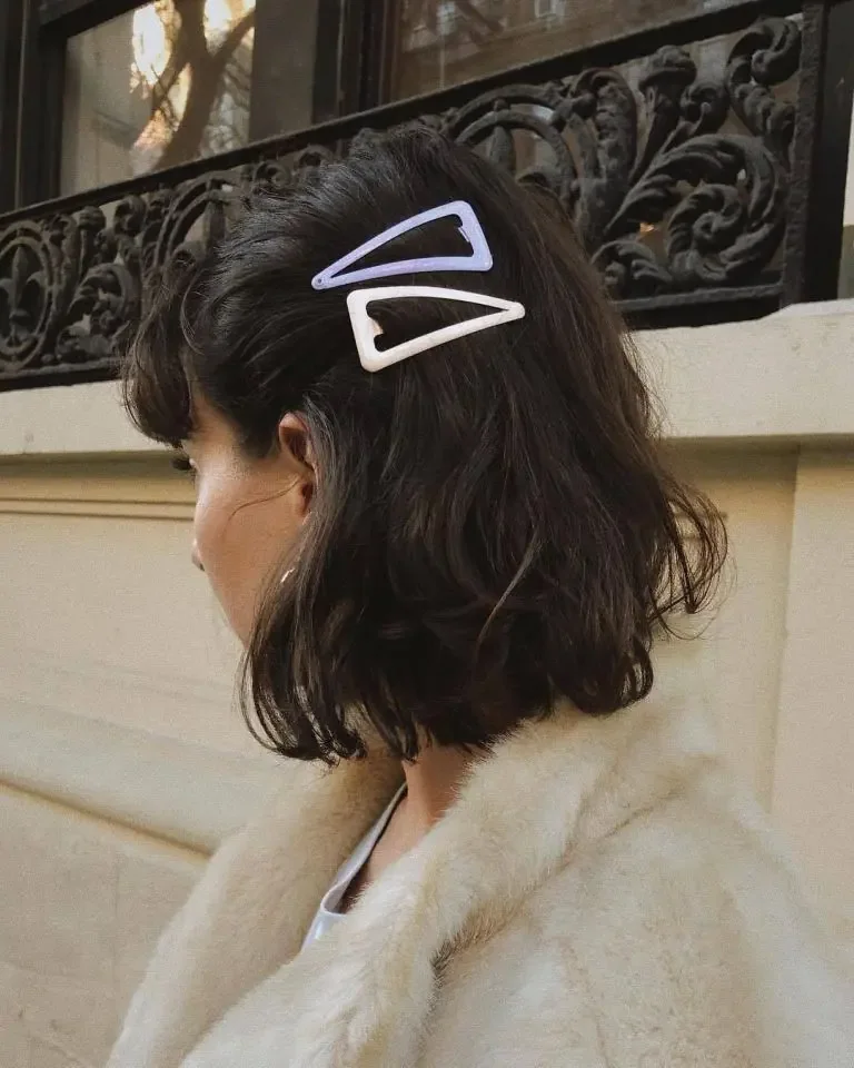 A wavy dark bob is pinned back on one side with two pale statement clips