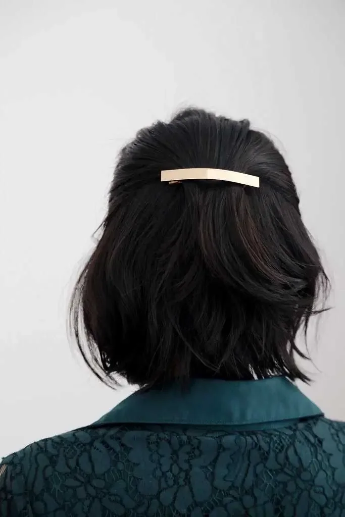 A softly wavy black bob is gathered into a clean half-up section with a slim barrette