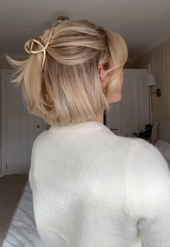 A tousled blonde bob is clipped half-up with a small beige claw clip near the crown