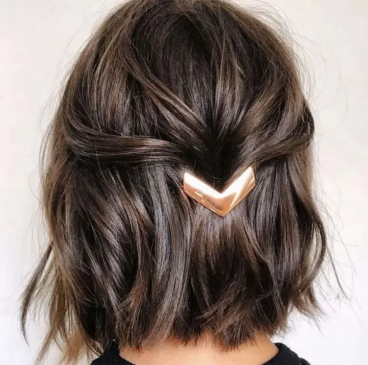 A short brunette bob is gathered at the back with a sculptural chevron-shaped barrette
