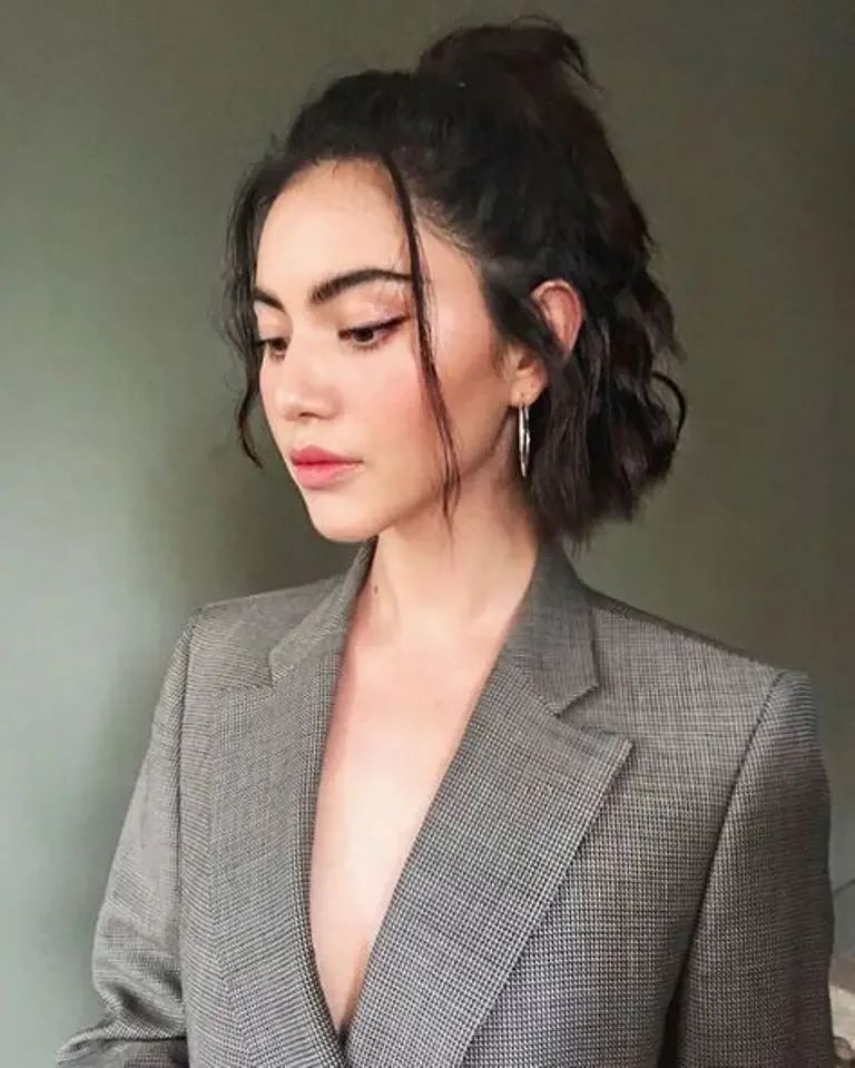 A brunette bob is lifted into a small half-up ponytail with loose face-framing pieces