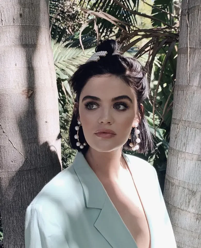 A dark wavy bob is pulled into a small top knot with curled pieces framing the face