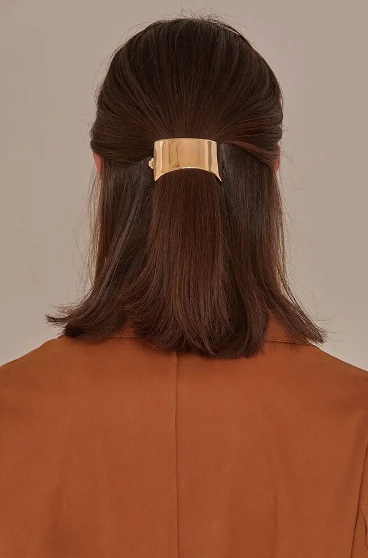 A straight auburn bob is pulled half-up beneath a broad brushed-gold barrette