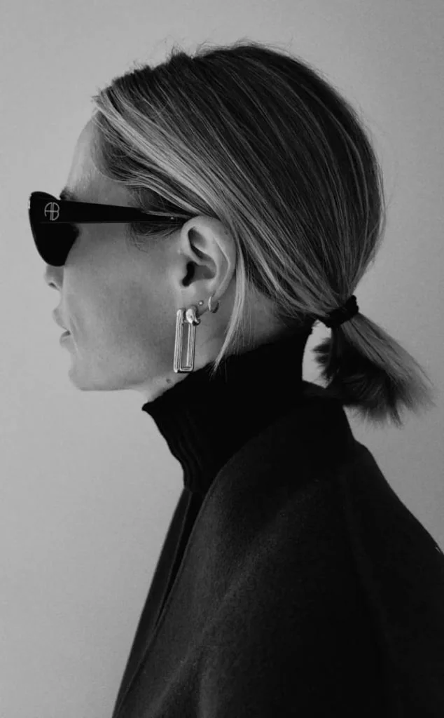 A sleek blonde bob is tied into a very small low ponytail beneath a clean center part