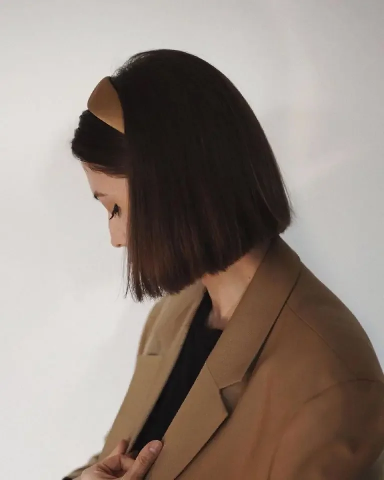 A glossy dark bob is held back with a wide black headband that blends into the hair