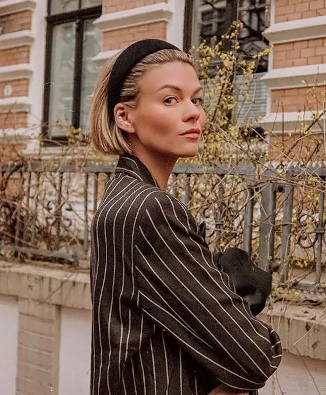 A brunette bob is styled behind a wide black padded headband with the ends tucked neatly
