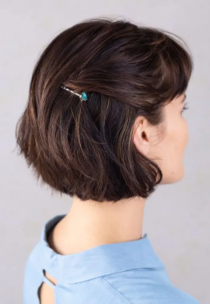 A short wavy brunette bob is swept back on one side with a small rhinestone hairpin